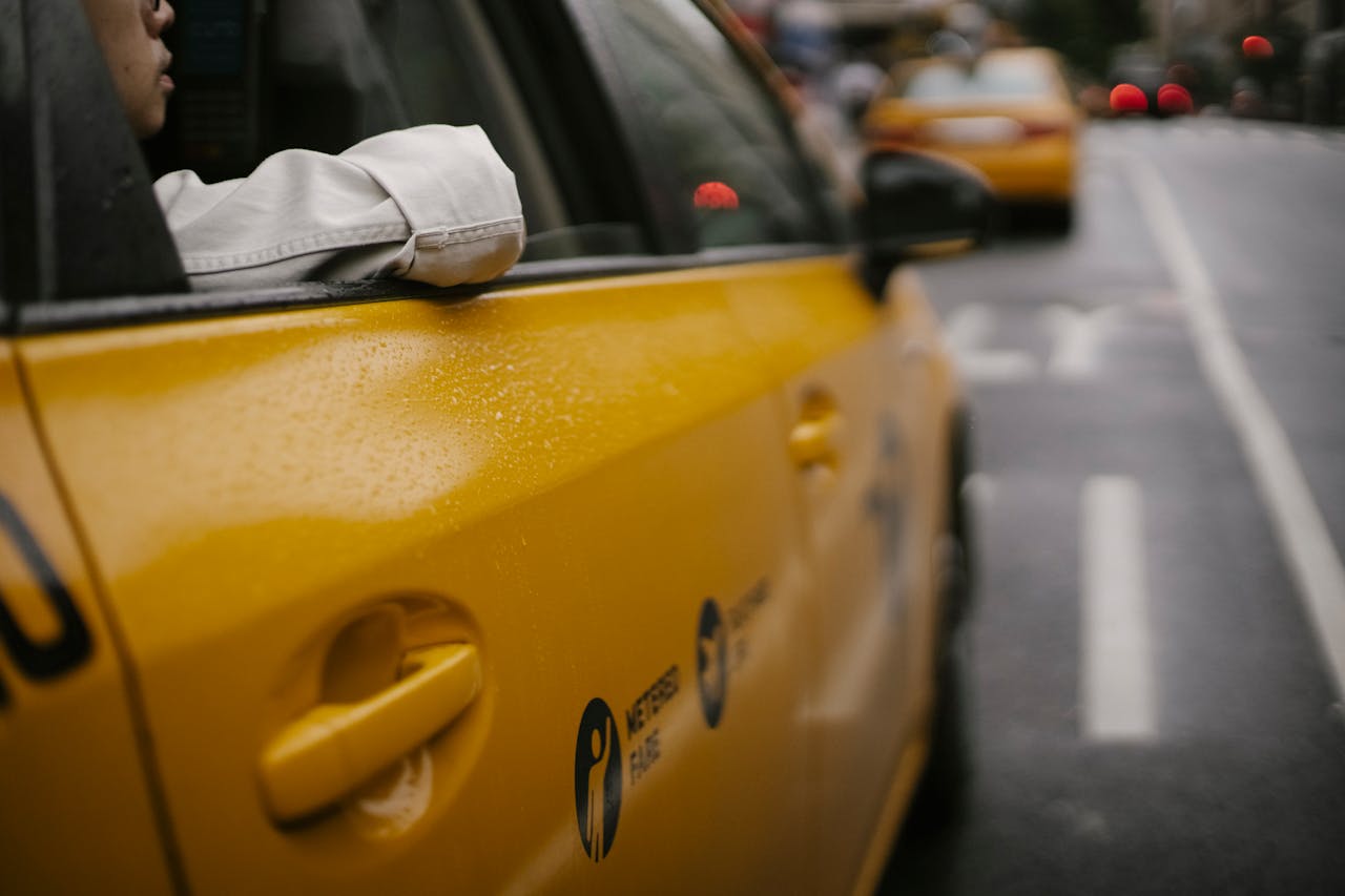A close-up of a yellow taxi with raindrops in an urban street setting, highlighting city life.