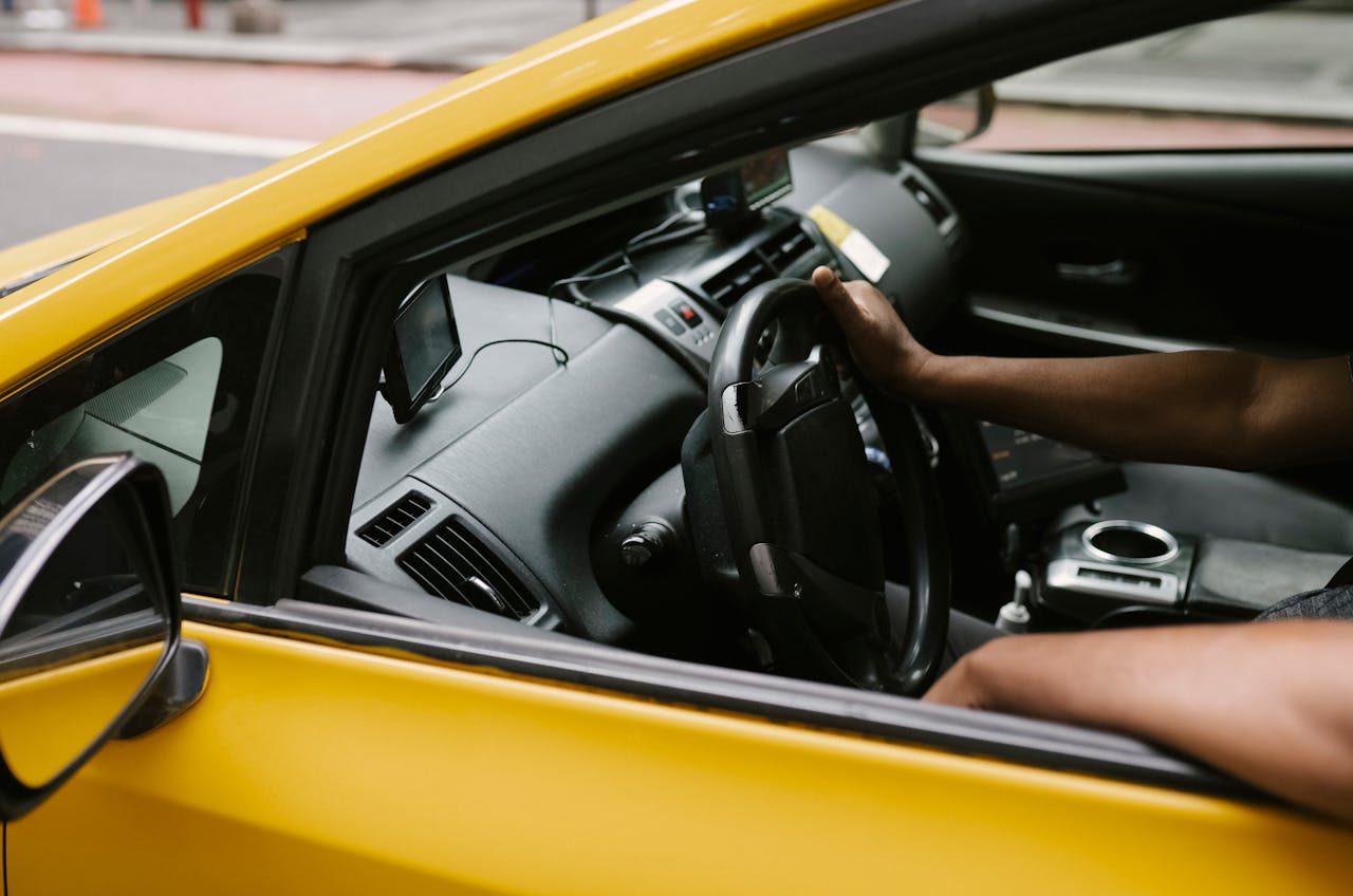 Close-up shot of a taxi driver steering a yellow cab on a city street.